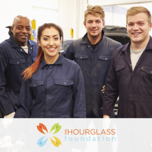 Four students enrolled in an automotive technology trade program, smiling at the camera